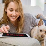 Persoon ontspant op de bank met een tablet en kijkt een film in de woonkamer